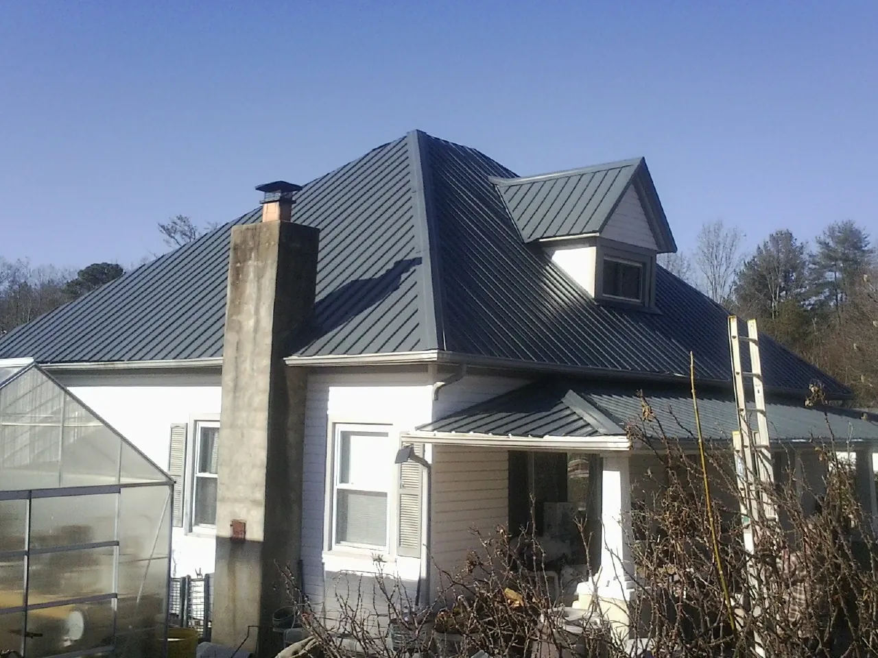 Dark blue standing seam metal roof on a white farmhouse with dormer — Slate & Tile Roof Repair by Roofing Brothers in Holdingford