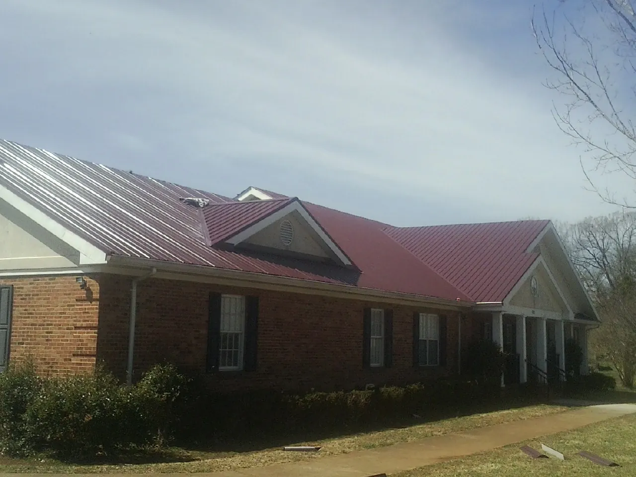Red metal roof with gabled entries on a long brick building, from a Hail Damage Roof Repair job in Holdingford