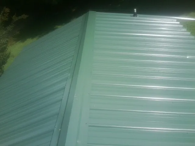 New green metal panels meeting at the ridge of a roof — Flat Roof Repair work by our crew in Holdingford