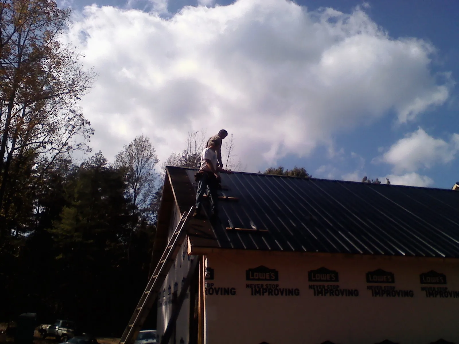 Roofer fastening dark metal panels high against a cloudy sky, from a Roof Inspection job in Holdingford