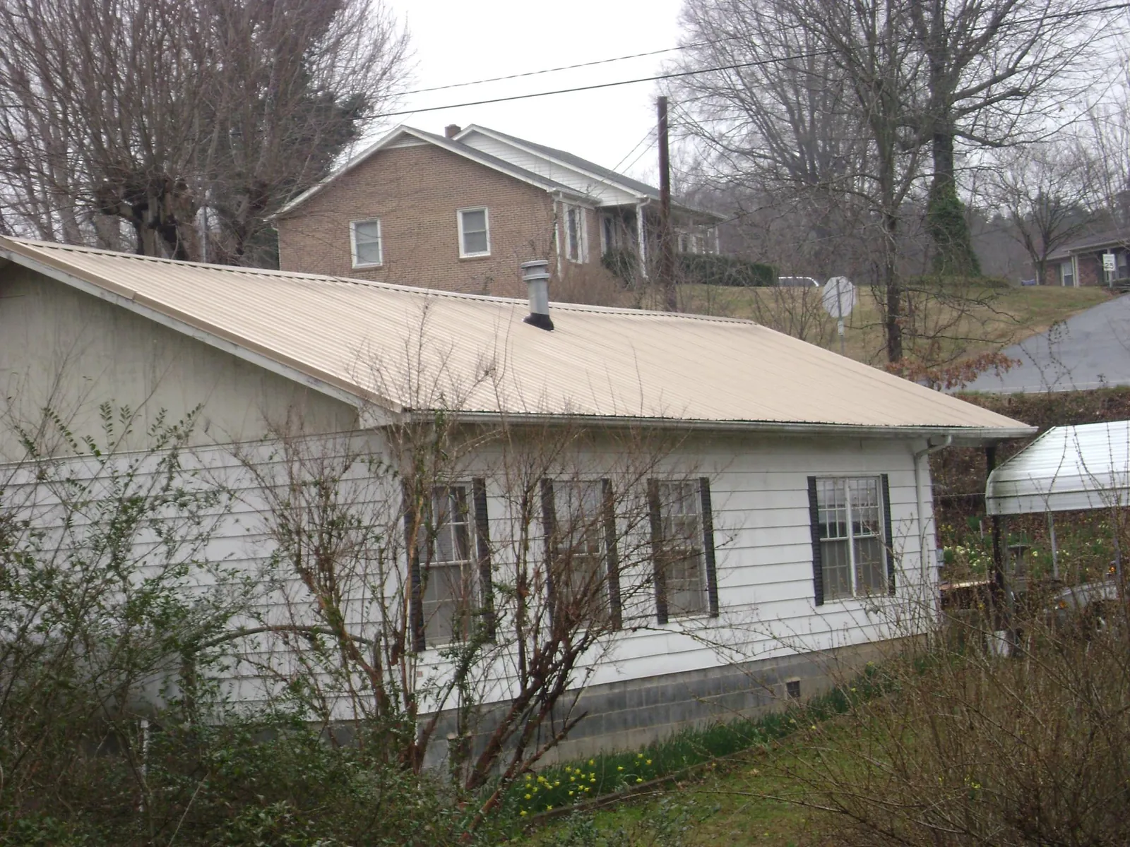 Tan metal roof on a white sided house set into a hillside — Commercial Roofing by Roofing Brothers in Holdingford