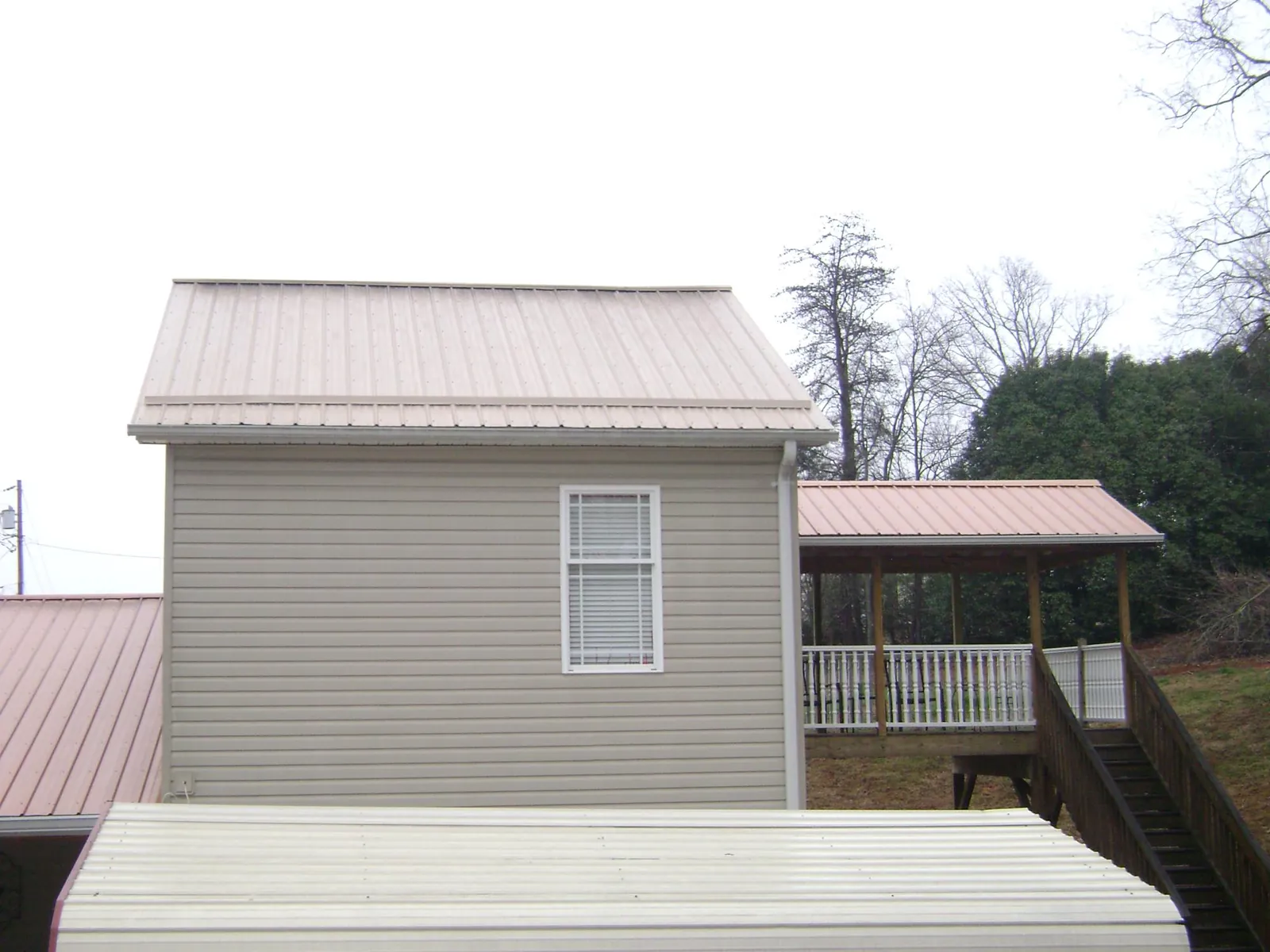 Tan metal roofs on a two story addition and attached porch, from a Roof Replacement job in Holdingford